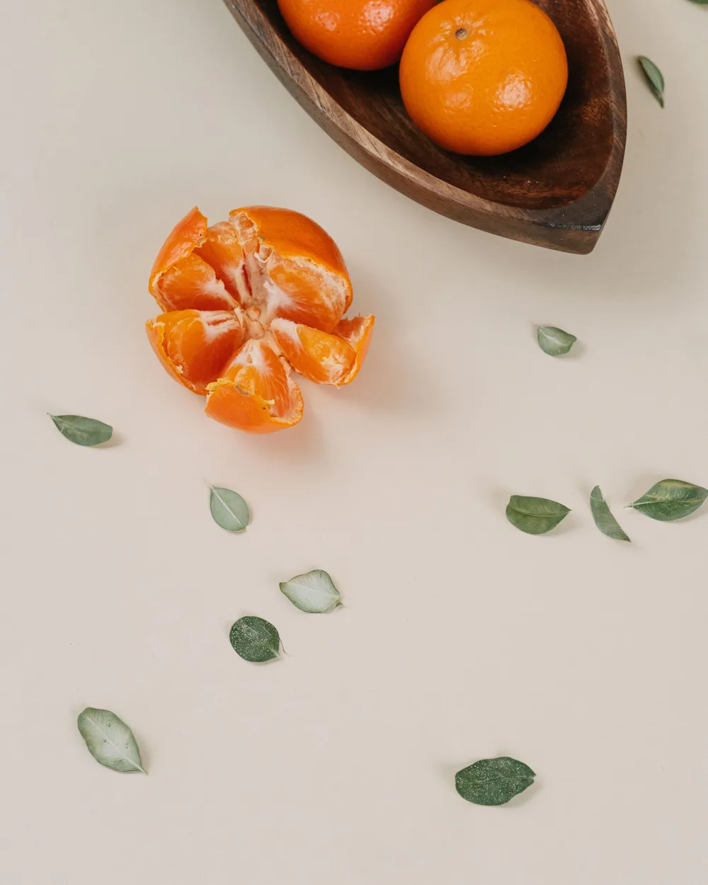 A peeled clementine opened into its segments, beside a bowl of whole clementines